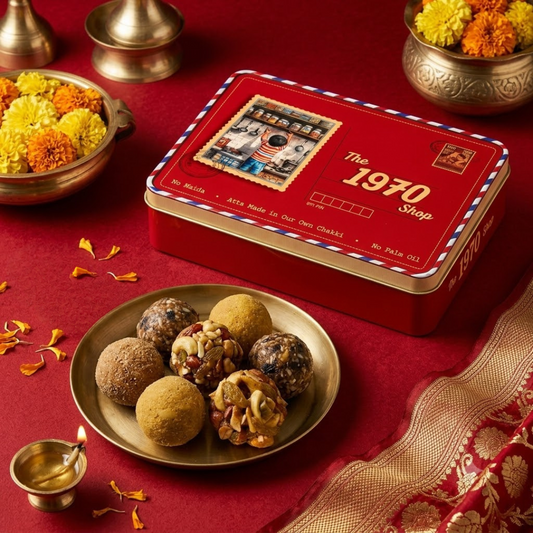 Assorted laddoos on a brass plate in front of The 1970 Shop tin, with marigolds and a diya