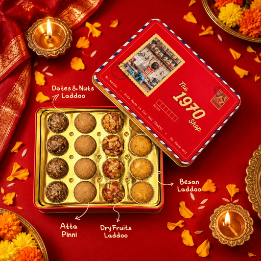 Assorted Laddoo tin open with Dates & Nuts Laddoo, Atta Pinni, Dry Fruit Laddoo and Besan Laddoo, among diyas and marigolds